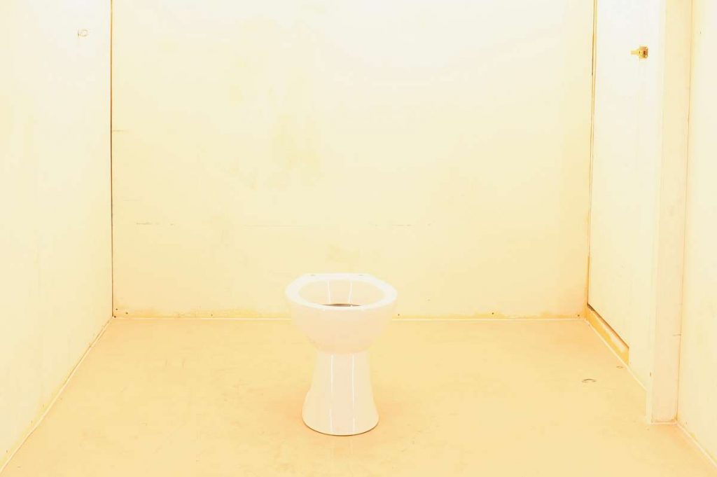 A toilet in the middle of an otherwise bare room, highlighted in harsh white light.