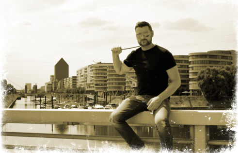Der dominus alias Master André in T-Shirt und Jeans vor der Kulisse des Duisburger Hafen zu Beginn seiner Karriere.